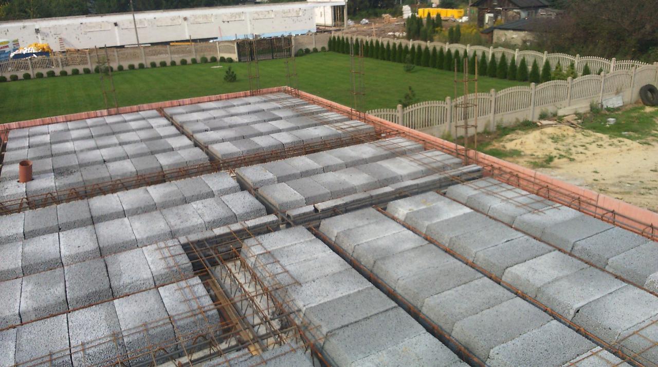 Widok z góry na strop Teriva w trakcie budowy z widocznymi belkami, pustakami i zbrojeniem, na tle zadbanego trawnika i ogrodzenia.