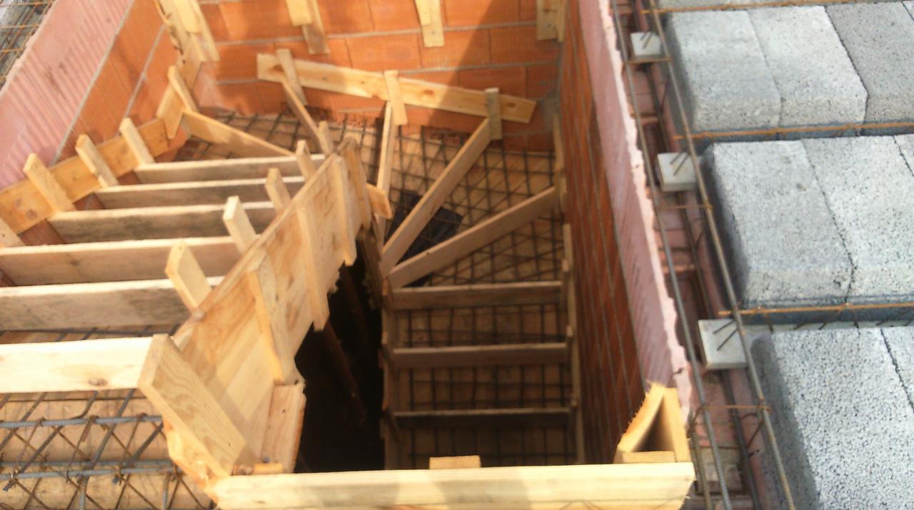Konstrukcja drewniana szalunku schodów na etapie budowy, widoczne zbrojenie i fragment murowanej ściany z pustaków ceramicznych.