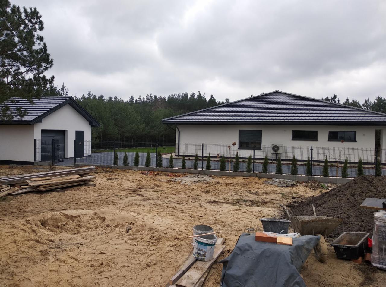 Niedawno wybudowany dom jednorodzinny z garażem, widok z terenu budowy, widoczne materiały budowlane i narzędzia.