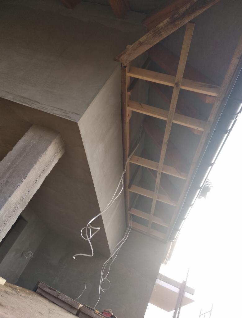 Surowy stan poddasza z widoczną drewnianą konstrukcją więźby dachowej, otynkowanymi ścianami i zwisającymi kablami elektrycznymi.