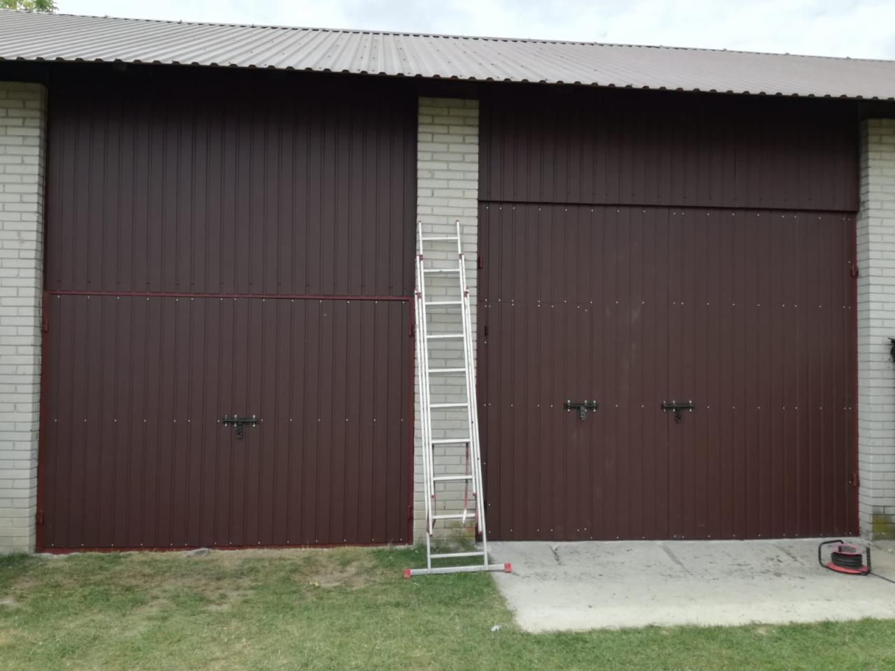 Dwa brązowe, metalowe garaże z białej cegły z widoczną drabiną aluminiową i zielonym trawnikiem z przodu.