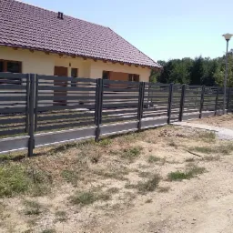 Nowoczesne, poziome ogrodzenie panelowe w kolorze antracytowym z betonową podmurówką, widoczne na tle domu z brązowym dachem i lampą uliczną.