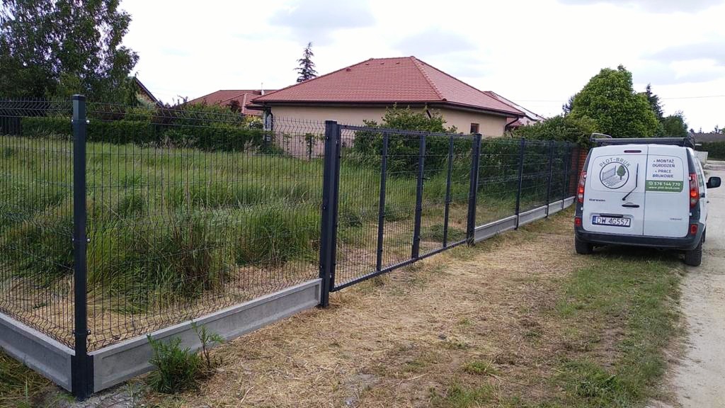 Zamontowane ogrodzenie panelowe z podmurówką betonową, widoczny fragment posesji z zarośniętym trawnikiem i samochód dostawczy firmy montującej ogrodzenia.
