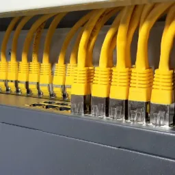 Rząd żółtych kabli Ethernet podłączonych do panelu krosowniczego w szafie rack, widoczne oznaczenia kabli FTP.