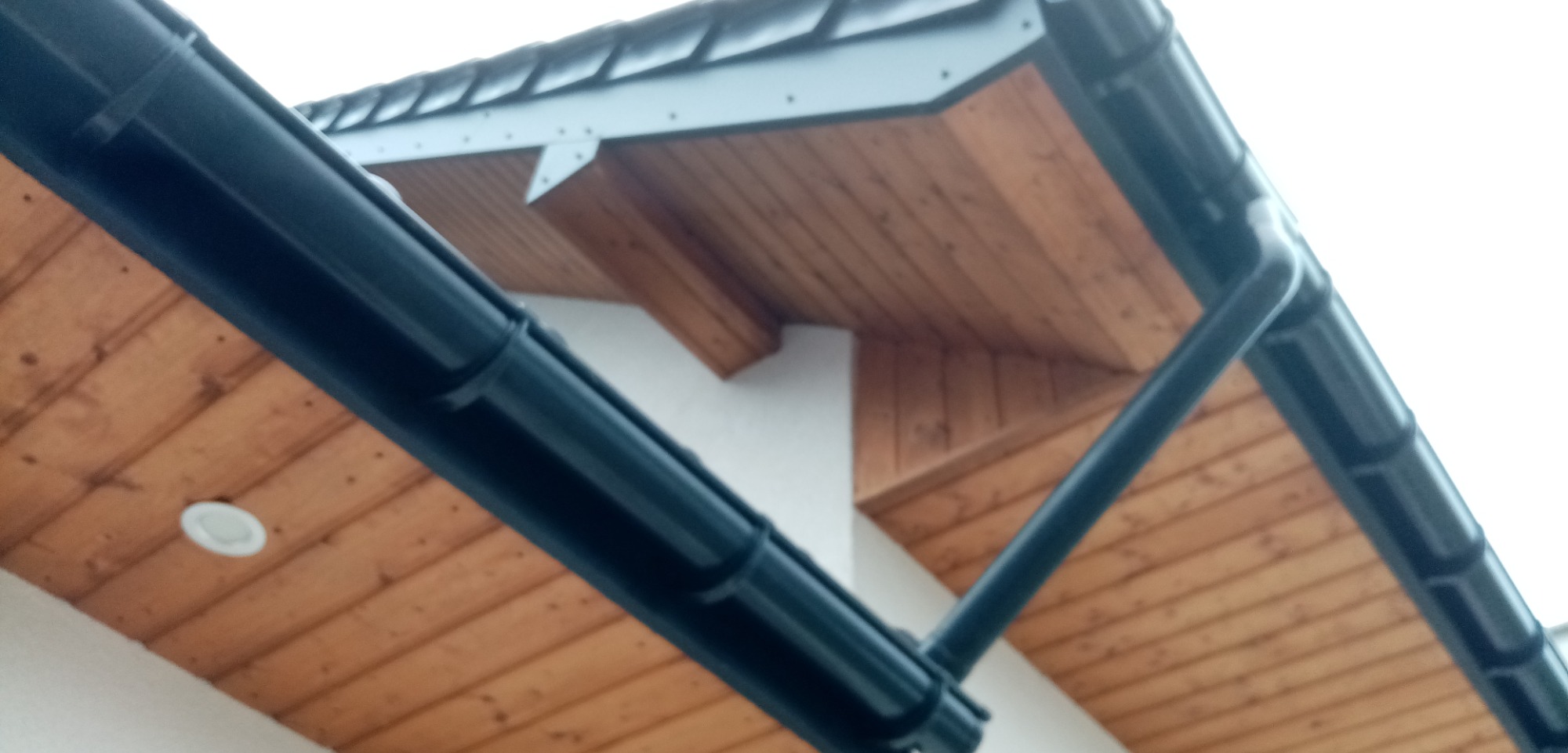 Fragment podbitki dachowej z drewnianą boazerią i zamontowanym oświetleniem punktowym oraz fragment orynnowania w kolorze grafitowym.