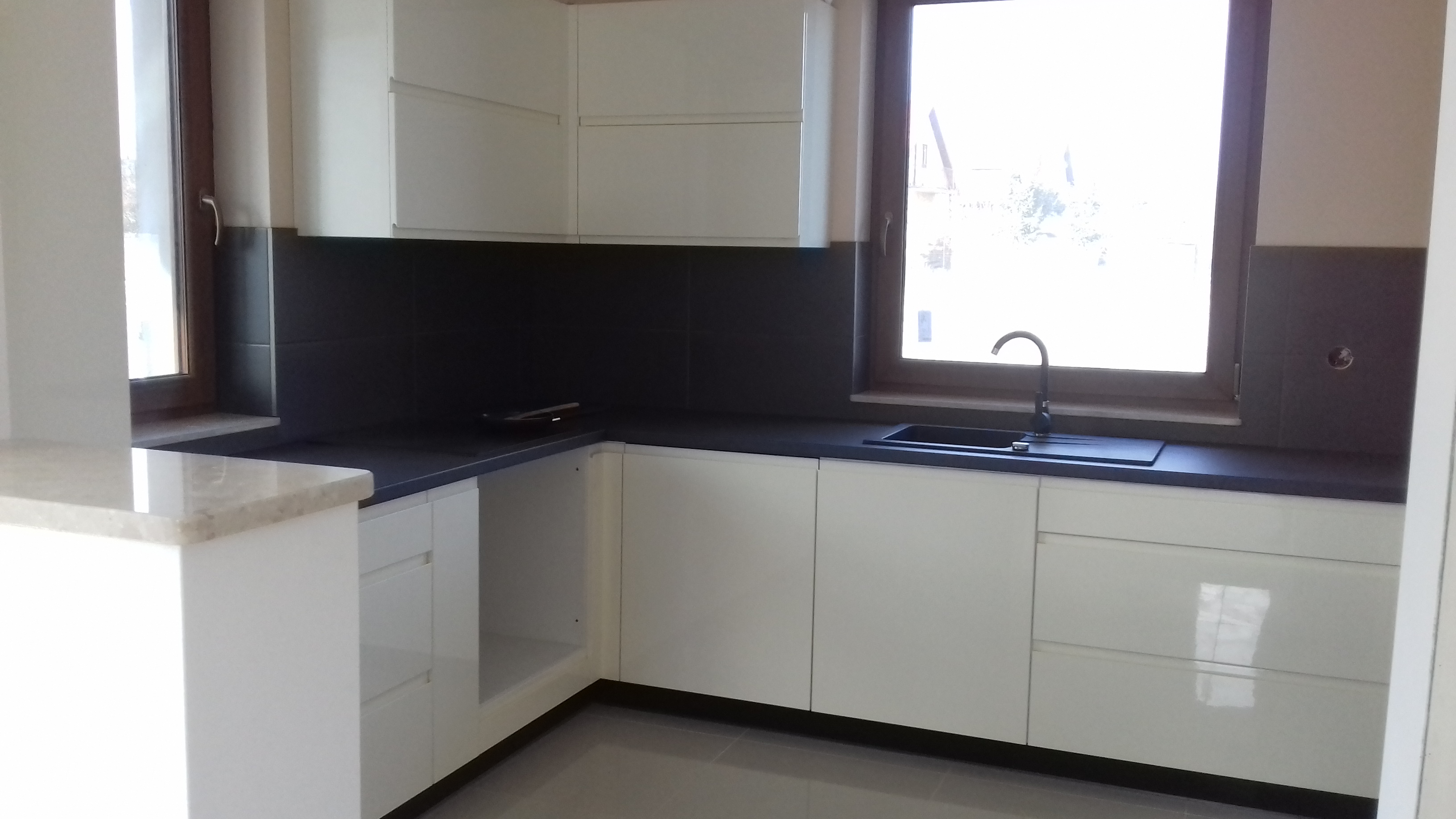 Nowoczesna kuchnia z białymi szafkami i czarnym blatem w Pęgowie, widok na okno i zlewozmywak.
