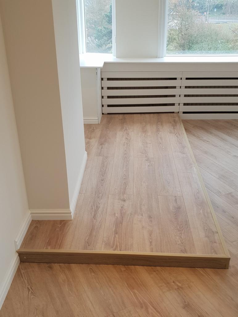 Wykończona podłoga z paneli w odcieniach drewna, z widocznymi listwami przypodłogowymi i przejściowymi, w jasnym wnętrzu w Ostrowi Mazowieckiej.