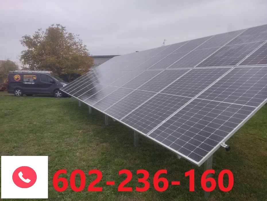 Panel fotowoltaiczny na trawie, z firmowym vanem w tle i numerem telefonu na pierwszym planie. Instalacja w pochmurny dzień.