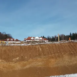 Prace ziemne pod budowę domu z użyciem niwelatora, widoczny wykop i częściowo ośnieżony teren.