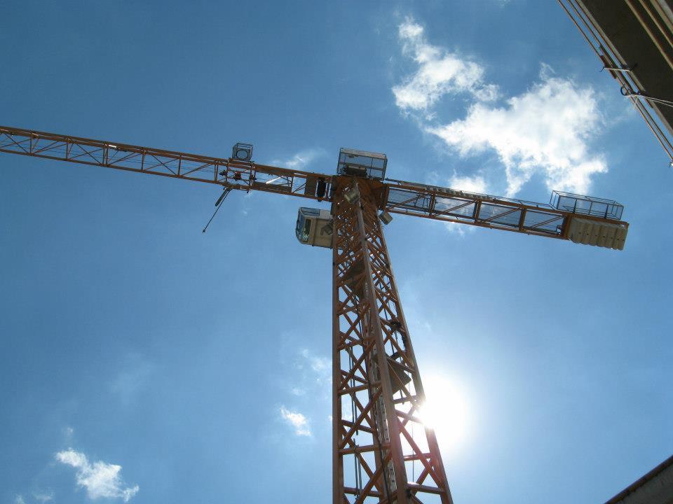 Żuraw budowlany z pomarańczowej kratownicy na tle błękitnego nieba z białymi obłokami, widok z dołu w słoneczny dzień.