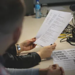 Uczestnik szkolenia z testem inteligencji emocjonalnej w rękach, obok arkusz z wizerunkami twarzy, na stole butelka wody i laptop.