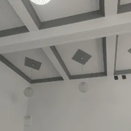 Jasne wnętrze z dekoracyjnym sufitem kasetonowym w odcieniach bieli i szarości, oświetlonym trzema nowoczesnymi lampami wiszącymi w kształcie kuli.