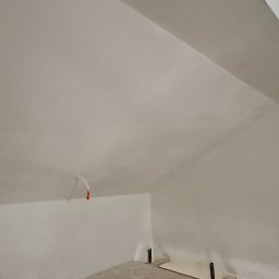 TermoGips Tomasz Buda - Wnętrze poddasza po gładziowaniu i malowaniu na biało. Widoczne skosy, fragment instalacji elektrycznej i elementy konstrukcyjne podłogi.