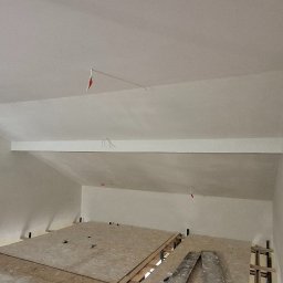 TermoGips Tomasz Buda - Poddasze po szpachlowaniu i malowaniu na biało, widoczne płyty OSB na podłodze i wystające kable. Ściany gładkie, jednolite, gotowe do dalszych prac wykończeniowych.