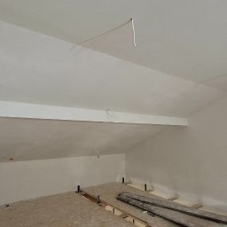 TermoGips Tomasz Buda - Poddasze po szpachlowaniu i malowaniu na biało, widoczne wystające kable i przygotowane podłoże pod podłogę. Skos dachu z belką.