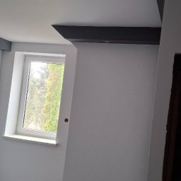 TermoGips Tomasz Buda - Wnętrze po remoncie: białe ściany, czarne elementy dekoracyjne na suficie, okno z widokiem na zieleń. Minimalistyczny design, świeżo pomalowane powierzchnie.