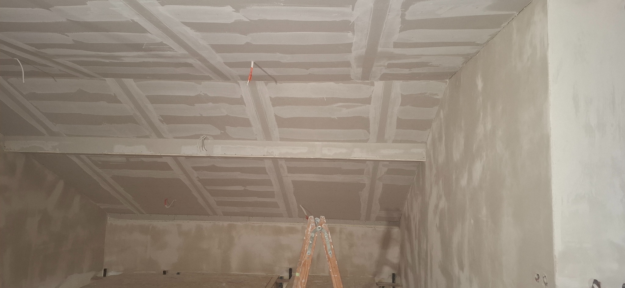 Sufit z płyt karton-gips, widoczne łączenia szpachlowane, drabina w pomieszczeniu. Prace wykończeniowe w trakcie realizacji.