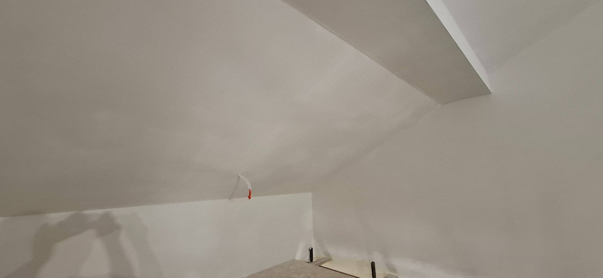 Wnętrze poddasza po gładziowaniu i malowaniu na biało. Widoczne skosy, fragment instalacji elektrycznej i elementy konstrukcyjne podłogi.