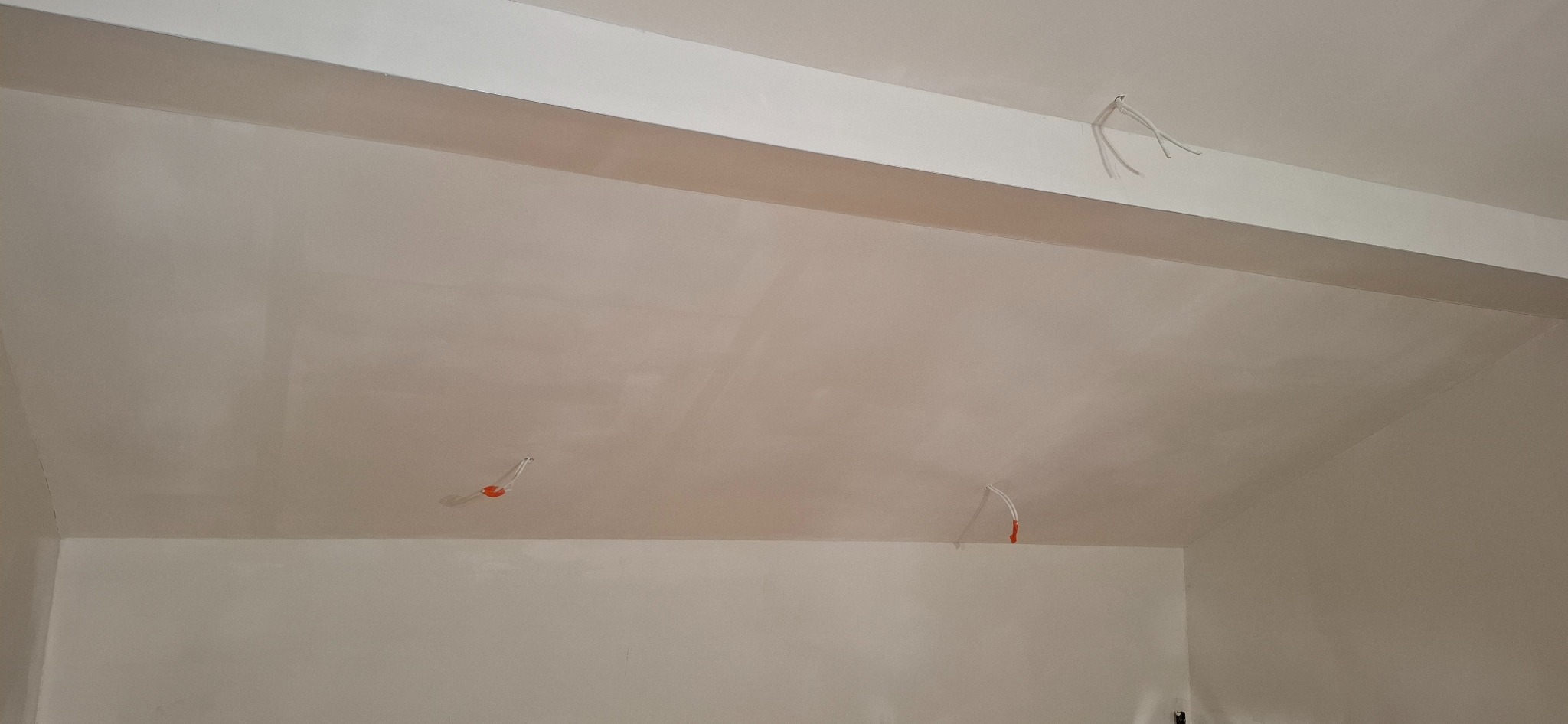 Gładka, biała powierzchnia sufitu po szpachlowaniu, z widocznymi przewodami elektrycznymi. Świeżo wykończone wnętrze, gotowe do dalszych prac.