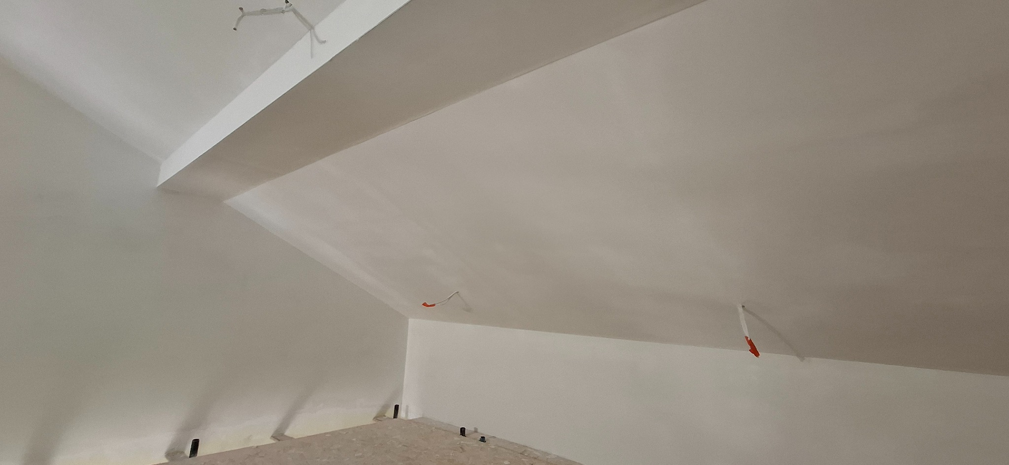 Wnętrze poddasza po szpachlowaniu i malowaniu na biało, widoczne gładkie ściany i sufit ze skosami, wystające kable elektryczne.