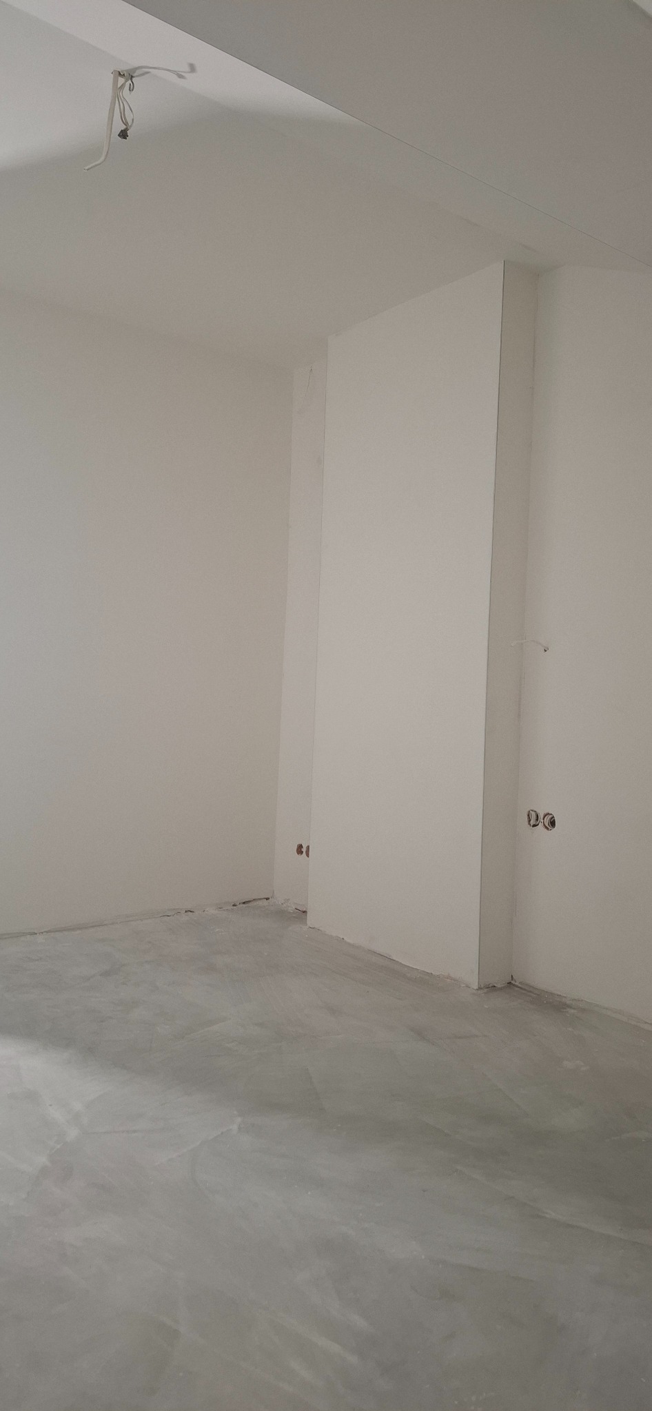 Wnętrze w trakcie prac wykończeniowych: gładkie, białe ściany, szara wylewka na podłodze, widoczne puszki elektryczne. Minimalistyczny kadr, surowy stan.