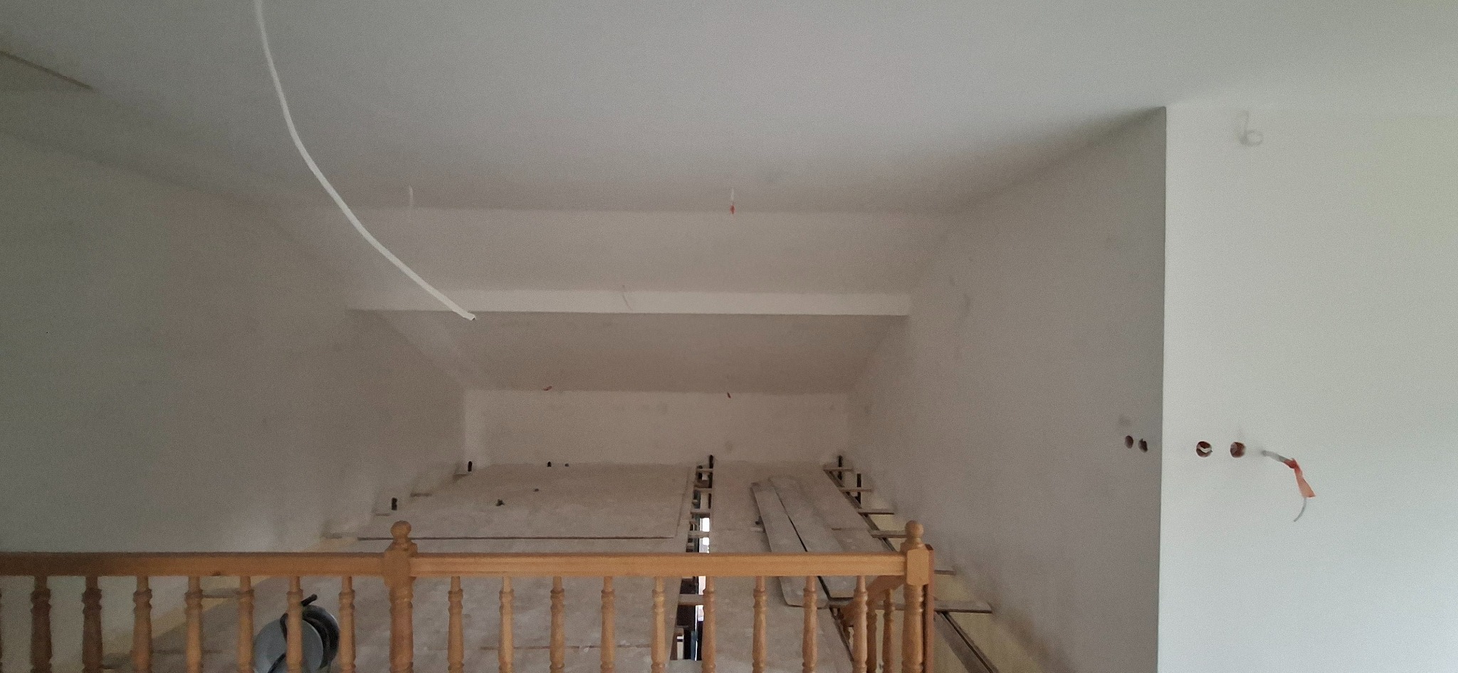 Poddasze w trakcie prac wykończeniowych: widoczne stelaże pod podłogę, przewody elektryczne wystające ze ścian, surowe ściany przygotowane do dalszych prac.