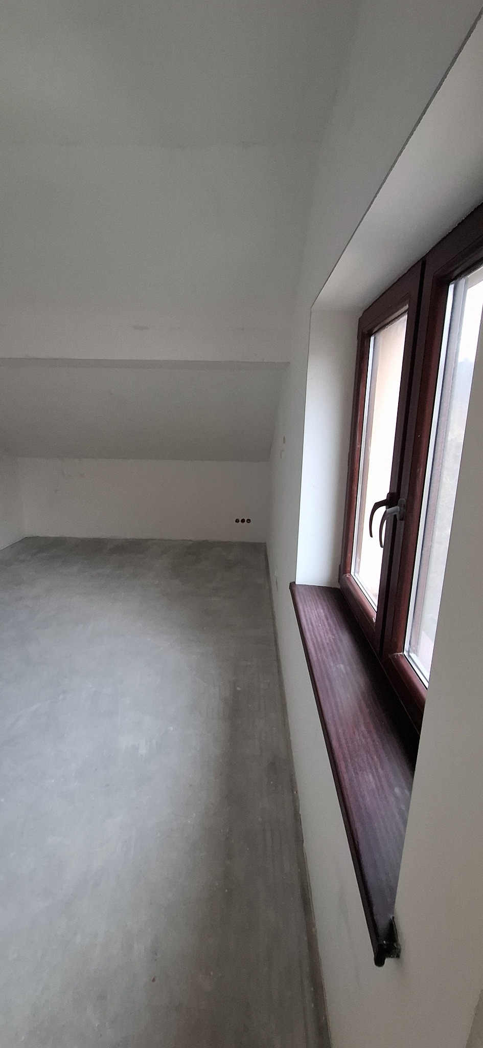 Poddasze po szpachlowaniu i gładziowaniu, przygotowane do malowania. Widoczne gładkie ściany, sufit ze skosem i okno z drewnianą ramą.