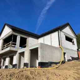 W.BRAŚ Nadzory Budowlane - Budowa domu jednorodzinnego w Wieliczce w stanie surowym otwartym, widok z dołu na tle błękitnego nieba z smugami kondensacyjnymi. Żółty wąż na ziemi.