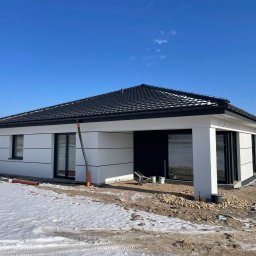 W.BRAŚ Nadzory Budowlane - Nowoczesny, parterowy dom jednorodzinny z czarnym dachem i białymi ścianami w zimowej scenerii. Widoczne detale wykończeniowe i teren wokół budynku w trakcie prac.