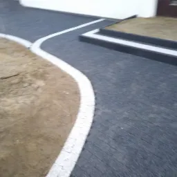 Ułożona ciemnoszara kostka brukowa z białym obramowaniem, tworząca ścieżkę i schody wejściowe do budynku.