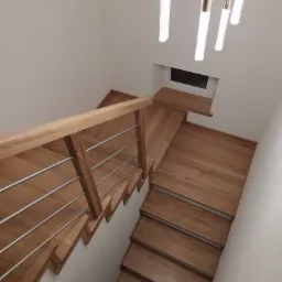 Nowoczesne drewniane schody z metalową balustradą, widok z góry, oświetlone przez designerską lampę wiszącą z kryształowymi elementami.