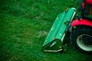 Traktor z zielonym kosiarką rotacyjną na trawniku, widoczne ślady koszenia.
