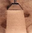 Fragment tekstylnej lampy wiszącej o trapezowym abażurze w beżowym odcieniu, na tle ściany o fakturze płótna.