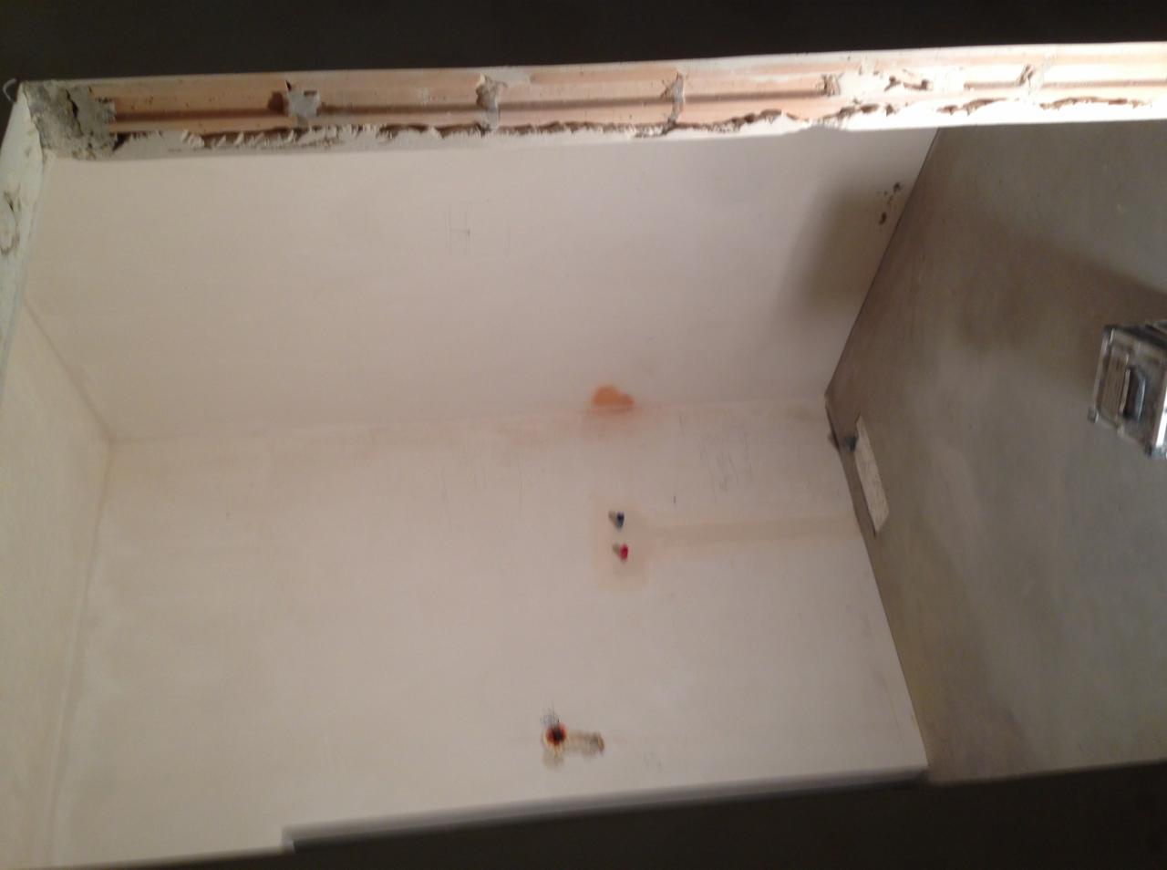 Surowy stan łazienki w trakcie prac: ściany przygotowane do położenia płytek, widoczne instalacje wodne, sufit z odsłoniętą konstrukcją, fragment podłogi w surowym betonie.