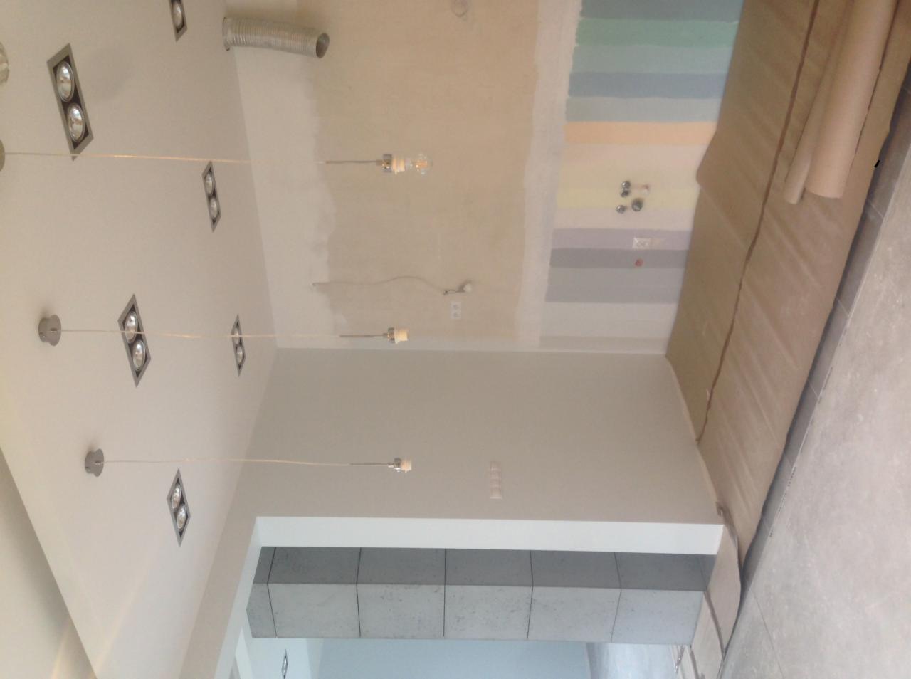 Wnętrze w trakcie prac wykończeniowych: surowa ściana z próbkami kolorów farb, zabezpieczona podłoga, widoczne instalacje elektryczne i oświetlenie punktowe.