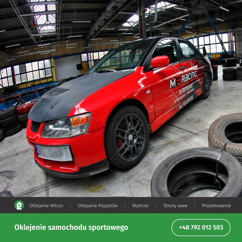 Czerwony samochód sportowy z grafitową maską, oklejony reklamą M Racing, stoi na tle opon w hali kartingowej.