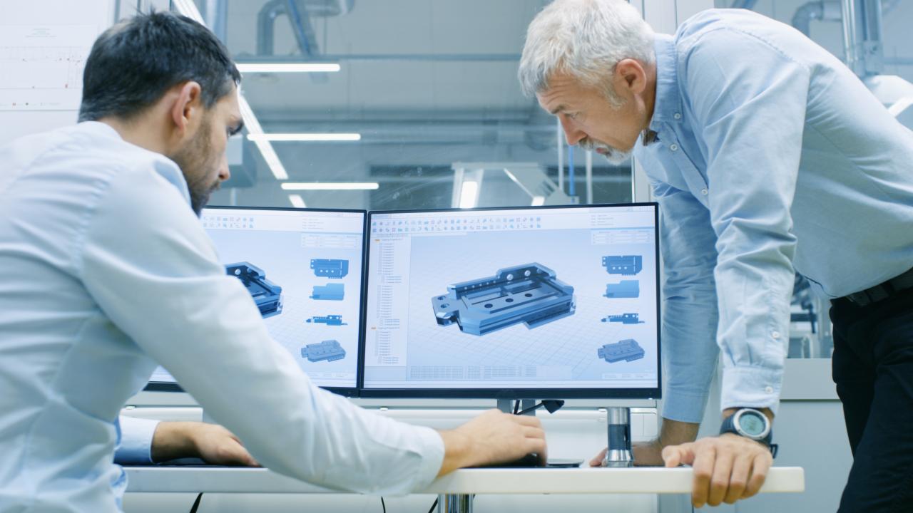 Dwóch inżynierów analizuje model 3D metalowej części na dwóch monitorach w jasnym, nowoczesnym laboratorium.