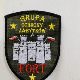 Naszywka z haftowanym motywem fortu, flagami Polski i napisem 'Grupa Ochrony Zabytków FORT' na oliwkowym tle.