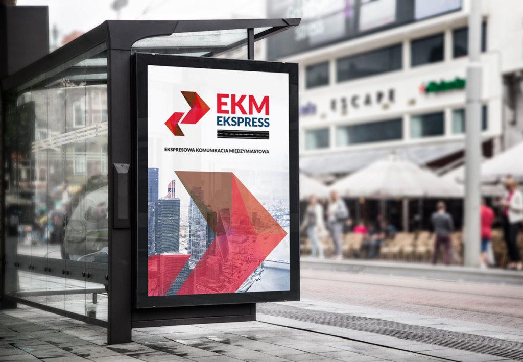 Billboard na przystanku autobusowym z reklamą firmy EKM Ekspress, prezentujący logo i hasło 'Ekspresowa Komunikacja Międzymiastowa', z abstrakcyjnym tłem panoramy miasta w czerwieni, na tle...