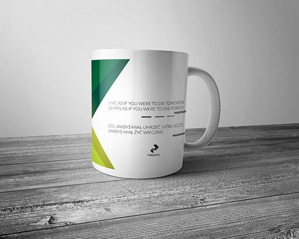 Biały kubek z nadrukiem motywacyjnego cytatu w języku angielskim i polskim, z zielono-żółtym gradientowym elementem graficznym, umieszczony na szarym drewnianym blacie na tle białej ściany.