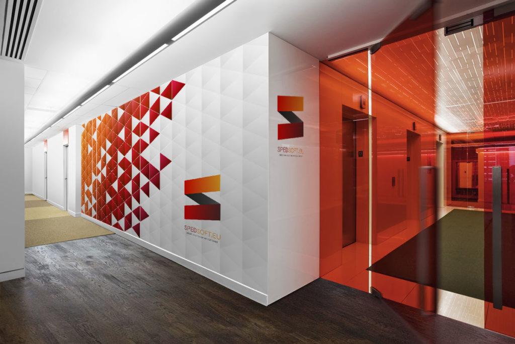 Wnętrze biura z geometrycznym wzorem w odcieniach czerwieni i pomarańczy na ścianie, logo firmy Spedsoft.eu i windami za szklaną, pomarańczową ścianą.