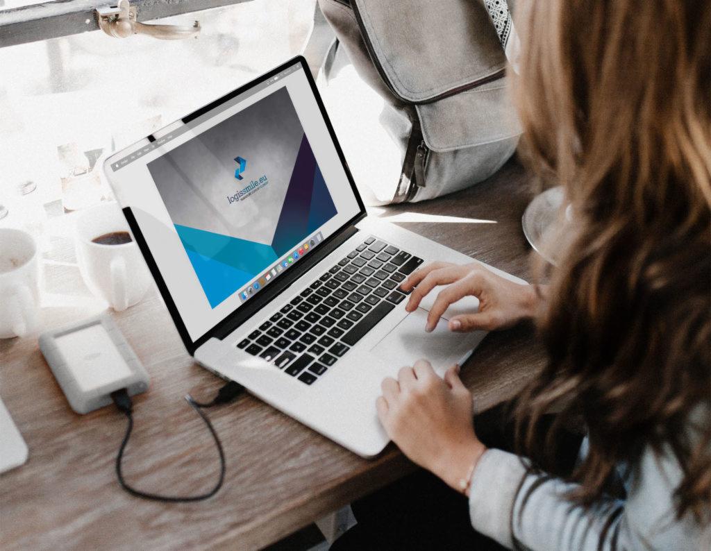 Kobieta pracuje na laptopie z wyświetlonym logo firmy logissmile.eu, obok kubek z kawą i zewnętrzny dysk twardy.