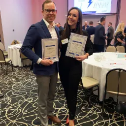 Uśmiechnięci uczestnicy szkolenia menedżerskiego Coach Studio prezentują certyfikaty ukończenia na tle sali konferencyjnej z projekcją 'Customized Personal Leadership'.