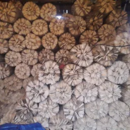 Stos drewnianych, okrągłych elementów do mocowania dachówki, ułożonych jeden na drugim w magazynie oświetlonym światłem słonecznym wpadającym przez szpary w ścianie.