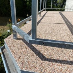 Styl Naprawa - Balkon wykończony drobnym kamieniem naturalnym, z metalową balustradą, widok z góry na fragment posadzki i barierki.