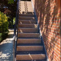 Styl Naprawa - Zewnętrzne schody z terazzo z metalową poręczą, przylegające do ceglanej ściany z cieniem rzucanym przez drzewo.