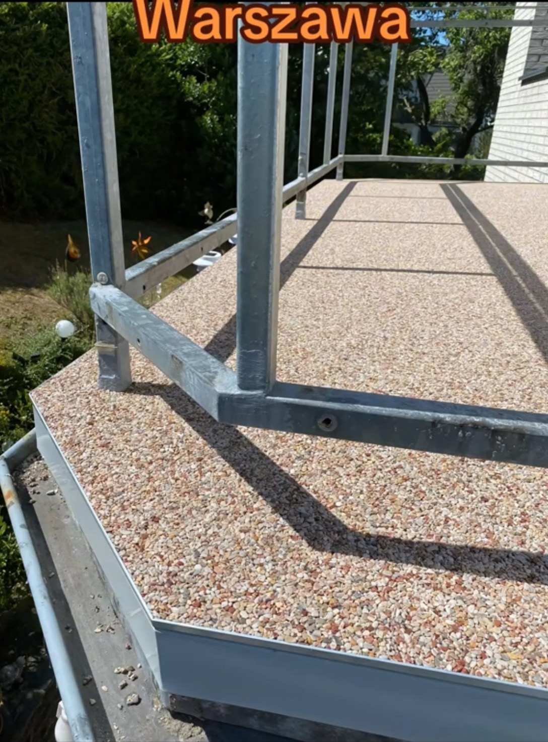 Balkon wykończony drobnym kamieniem naturalnym, z metalową balustradą, widok z góry na fragment posadzki i barierki.