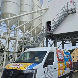 PRZEDSIĘBIORSTWO HANDLOWO USŁUGOWE Karolina WUZIEŃ - Renault Master z reklamą firmy Anhydryt Expert na tle silosów Holcim. Grafika w stylu komiksowym, numery kontaktowe i adres strony internetowej na karoserii.