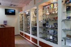 Wnętrze lokalu handlowego z przeszklonymi witrynami ekspozycyjnymi, widoczny fragment lady recepcyjnej i telewizor na ścianie.