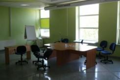 Wnętrze biurowe z dużym stołem konferencyjnym, krzesłami na kółkach, tablicą suchościeralną i oknami z widokiem na zieleń. Ściany pomalowane na jasnozielony kolor.